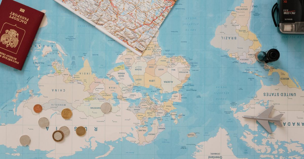Flat lay of a world map, passport, coins, and camera for travel planning.